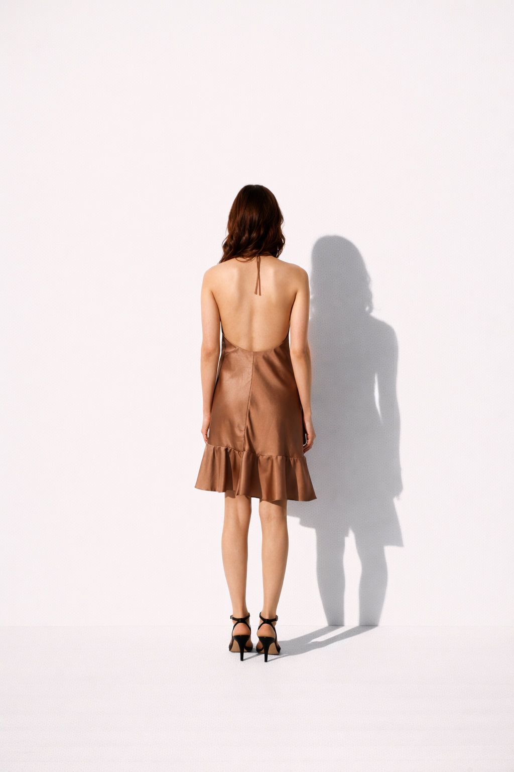 Woman wearing a brown satin dress with a backless design on a white background back